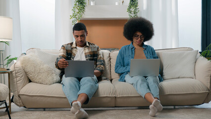 African American couple technology video game addict family with two laptops playing online on couch home woman work with laptop man computer working freelancers with computers on sofa separate ignore