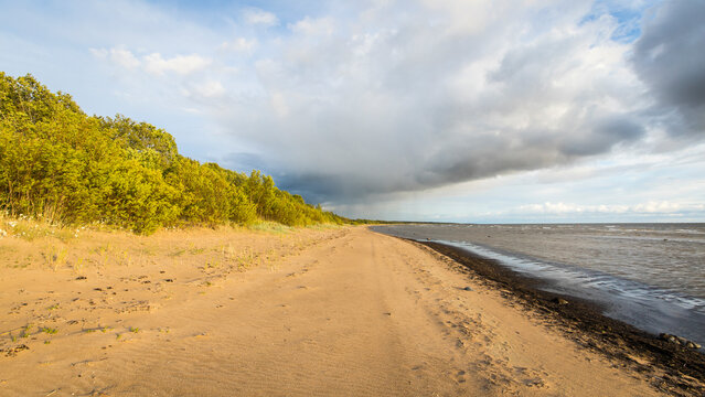 View of tranquil sandy beach and calm ocean under a picturesque sky with clouds, Paernu, Estonia.