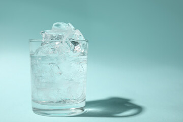 Refreshing water with ice in glass on turquoise background. Space for text