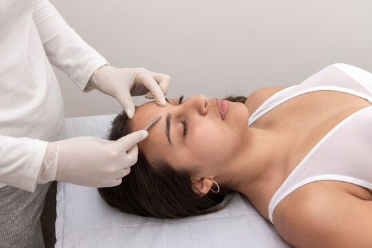 young woman on a table in a beauty center performing a beauty treatment for facial skin with a scalpel using the dermaplaning technique