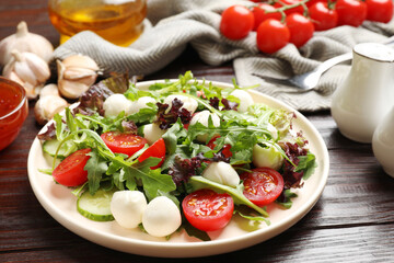 Tasty salad with arugula, lettuce, mozzarella cheese and vegetables on wooden table, closeup