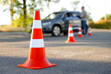 Examiner instructing student before exam at driving school test track, focus on traffic cone