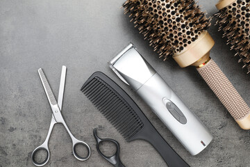 Professional hair clipper, different combs and scissors on grey surface, flat lay