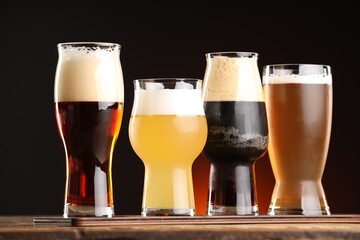Glasses with different types of beer on wooden table against dark background