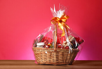 Wicker gift basket with wine on wooden table against pink background