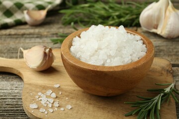 Sea salt in bowl, rosemary and garlic on wooden table, closeup