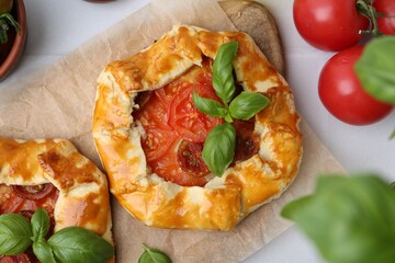 Tasty galettes with tomato and basil on white tiled table, flat lay