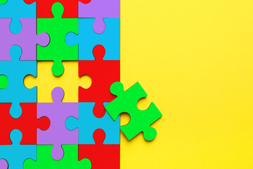 Many colorful puzzle pieces on yellow background, top view. Symbol of autism