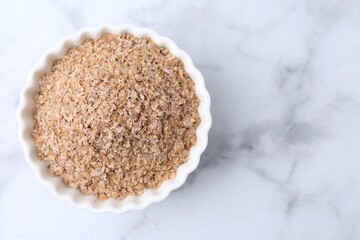 Buckwheat bran in bowl on white marble table, top view. Space for text