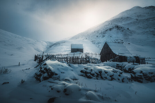 View of serene berizhdol barns in snowy landscape with rustic fence and mountains, Lepushe, Albania.