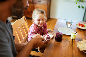 Father making breakfast for daughter with jam on toast