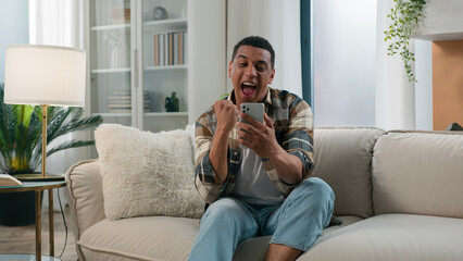 Surprised excited African American shocked man winner win smartphone achieve read good internet...