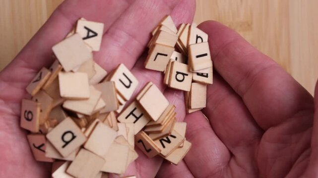 A person is holding wooden letters and numbers cupped in their hand. The letters and numbers fall through the person's fingers. Concept, literacy, numeracy, dyslexia, reading.