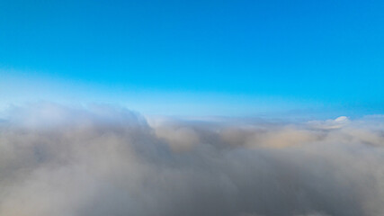A serene view of the early morning sun rising above a vast sea of clouds, with distant mountain peaks faintly visible on the horizon, creating a peaceful and ethereal landscape. Flying over the cloud