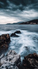 Fototapeta premium Moody Seascape with Smoothing Waves Crashing on Rocky Coastline at Twilight