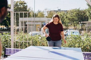 Happy young woman playing table tennis with African American man outdoors