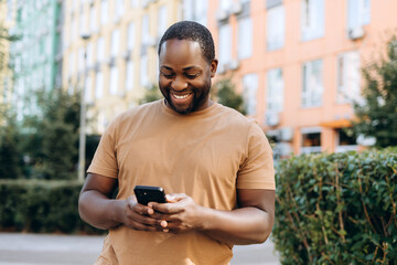 Smiling young African American man typing on the smartphone in the city