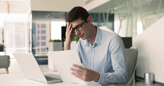 Frustrated man sit at desk holds paper notification with negative bad news, read about failure of project leading to potential financial losses, company layoffs or downsizing, bankruptcy or subpoena