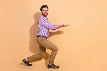 Full length photo of handsome young guy hold carry empty space dressed stylish striped formalwear isolated on beige color background