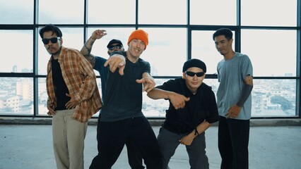 Multicultural hipster group looking at camera while perform break dancing at building with sky...