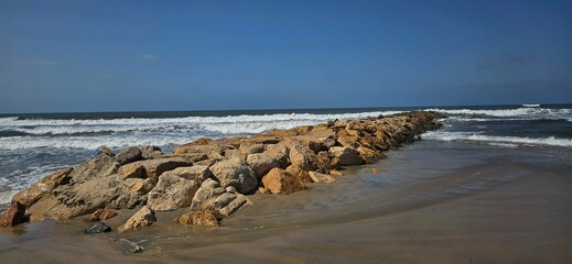 Scenic coastal landscape with large rock formations, clear blue water, and sandy beach.