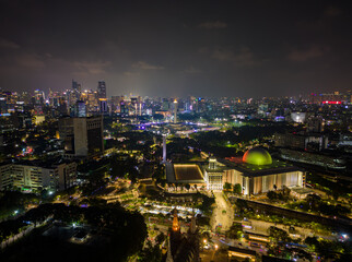 Fototapeta premium Aerial view of Jakarta city skyline with the illuminated Istiqlal Mosque and Jakarta Cathedral at night.