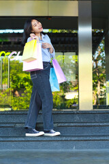 vertical shoot of laughing asian woman holding shopping bag walking on staircase in front of mall entrance