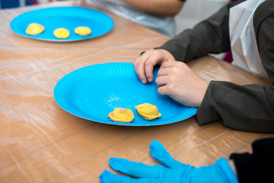 Children's hands preparing dumplings and ravioli dough during a cooking class. A detailed culinary workshop scene showing kids engaging with food and learning kitchen skills in a playful setting