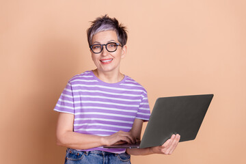Photo of charming pensioner woman wear striped stylish clothes use netbook isolated on beige color background