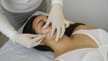 young woman on a table in a beauty center performing a beauty treatment for facial skin with a scalpel using the dermaplaning technique