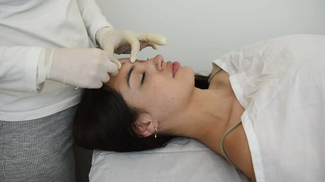 young woman on a table in a beauty center performing a beauty treatment for facial skin with a scalpel using the dermaplaning technique
