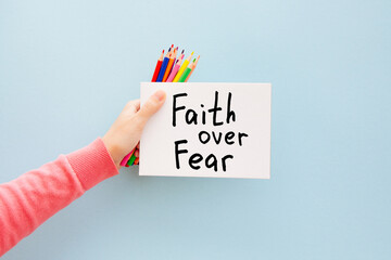 Faith over fear - woman hand with christian motivation text on light blue background