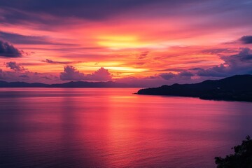 A vibrant sunset over the Andaman Sea, with hues of orange and pink reflecting on the calm waters, viewed from Windmill View Point in Phuket, Thailand.