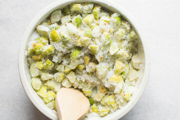 Overhead view of lime slices and sugar being mixed together in a white bowl, process of making lime cheong or lime syrup