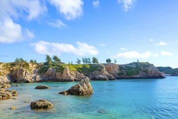 Fototapeta premium A scenic coastal landscape with turquoise waters, rocky cliffs, and a blue sky with fluffy white clouds