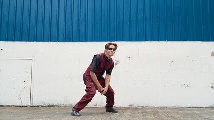 Handsome street dancer practicing break dancing at white back ground. Sport man wearing hip hop style while moving footsteps to music at street with blue background. Outdoor sport 2024. Hiphop.