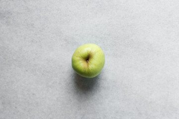 Overhead view of a whole green apple on a white granite countertop, top view of a crisp green apple on a white countertop