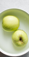 Overhead view of a whole green apple in a bowl of water, top view of a crisp green apple being washed in a white ceramic bowl