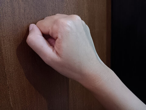 Woman hand knocking fist on wooden door.