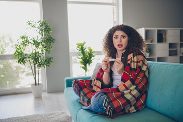 Photo portrait of curly haired young girl sitting comfortable couch wrapped checkered blanket sick staring thermometer measure at home