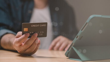 Close-up of hand holding credit card while using tablet on wooden table, symbolizing online shopping and digital transactions in modern lifestyle