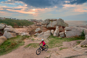 Fototapeta premium active senior woman cycling with her electric mountain bike at the rocky red granite cost next to Ploumanac'h, Côtes d'Armor,Brittany, France