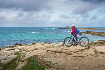 Fototapeta premium active senior woman cycling with her electric mountain bike at the rocky red granite cost next to Ploumanac'h, Côtes d'Armor,Brittany, France
