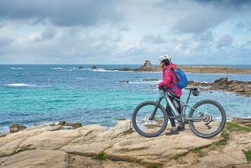 Obraz premium active senior woman cycling with her electric mountain bike at the rocky red granite cost next to Ploumanac'h, Côtes d'Armor,Brittany, France