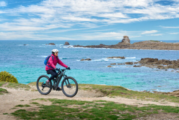 Obraz premium active senior woman cycling with her electric mountain bike at the rocky red granite cost next to Ploumanac'h, Côtes d'Armor,Brittany, France