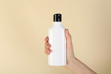 Woman with shampoo bottle on beige background, closeup