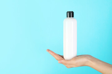 Woman with shampoo bottle on light blue background, closeup. Space for text