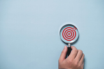Hand holding target board inside of magnifier glass for focus business objective on blue background...