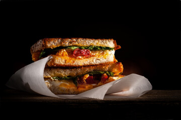 Delicious gourmet homemade sandwich with fried egg and melted cheese, tomato slices and basil leaves