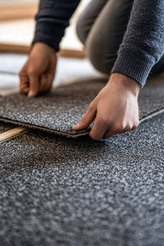 Close-up of hands installing self adhesive carpet tiles on living room floor in apartment home 